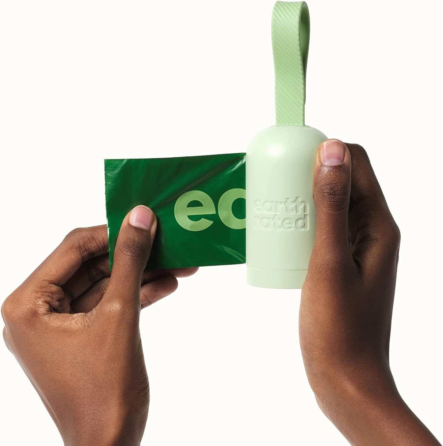 Hand holding a green dog poop bag being pulled from a light green, leash-attached dog poop bag holder.
