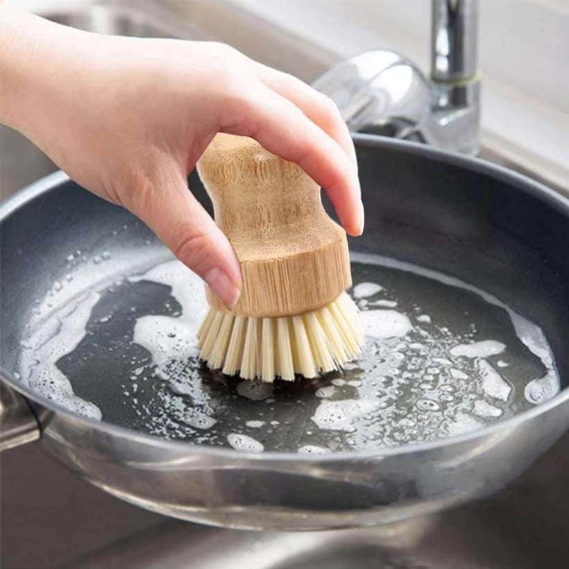 Eco-friendly bamboo cleaning brush scrubbing a pan in the kitchen sink.