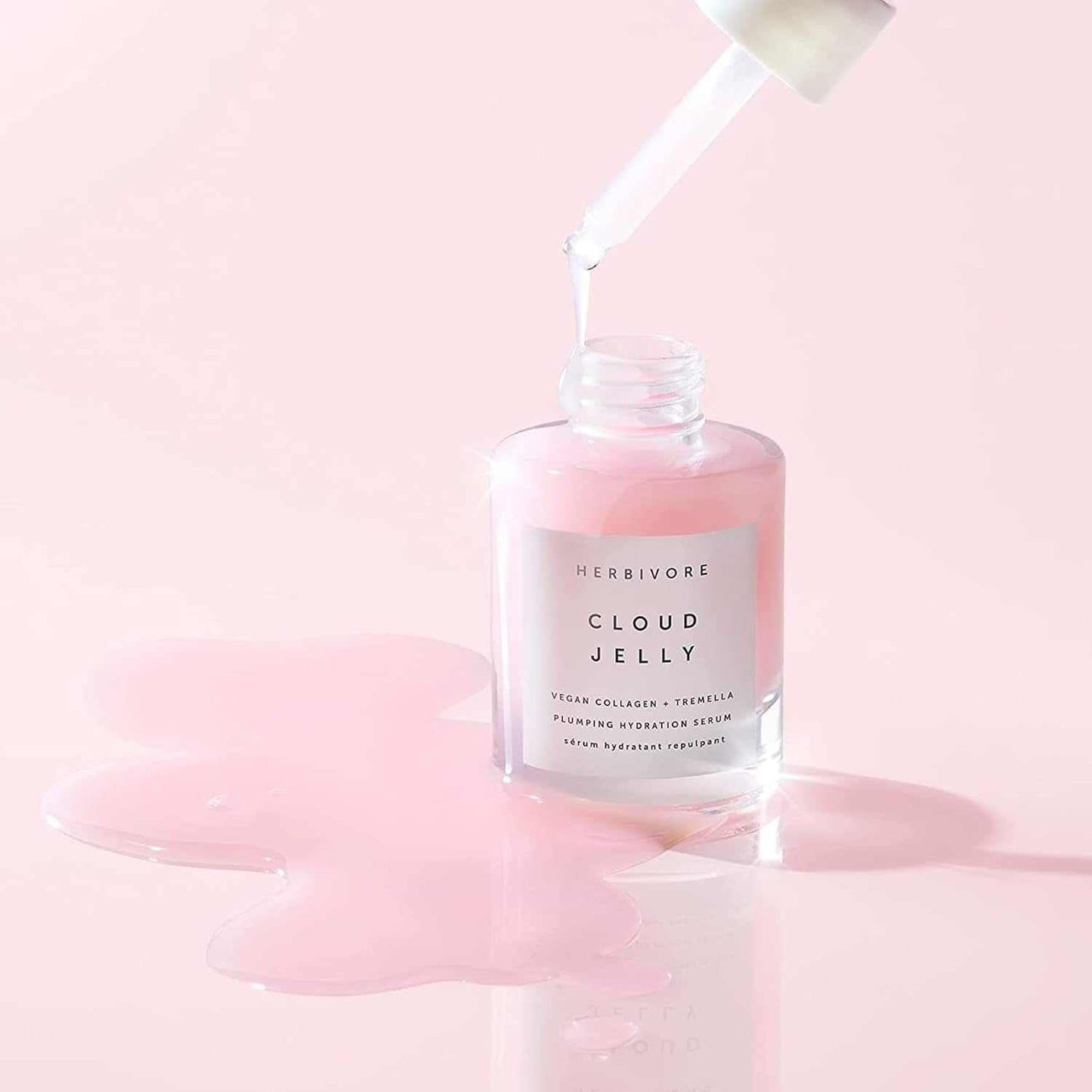 Cloud Jelly Plumping hydrating face serum with vegan collagen and Tremella mushroom in a clear bottle with pink jelly texture spilling on a pale pink surface