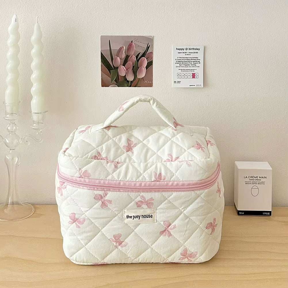 Quilted floral makeup bag with bow accent, durable cotton design, spacious, portable, secure zipper closure.