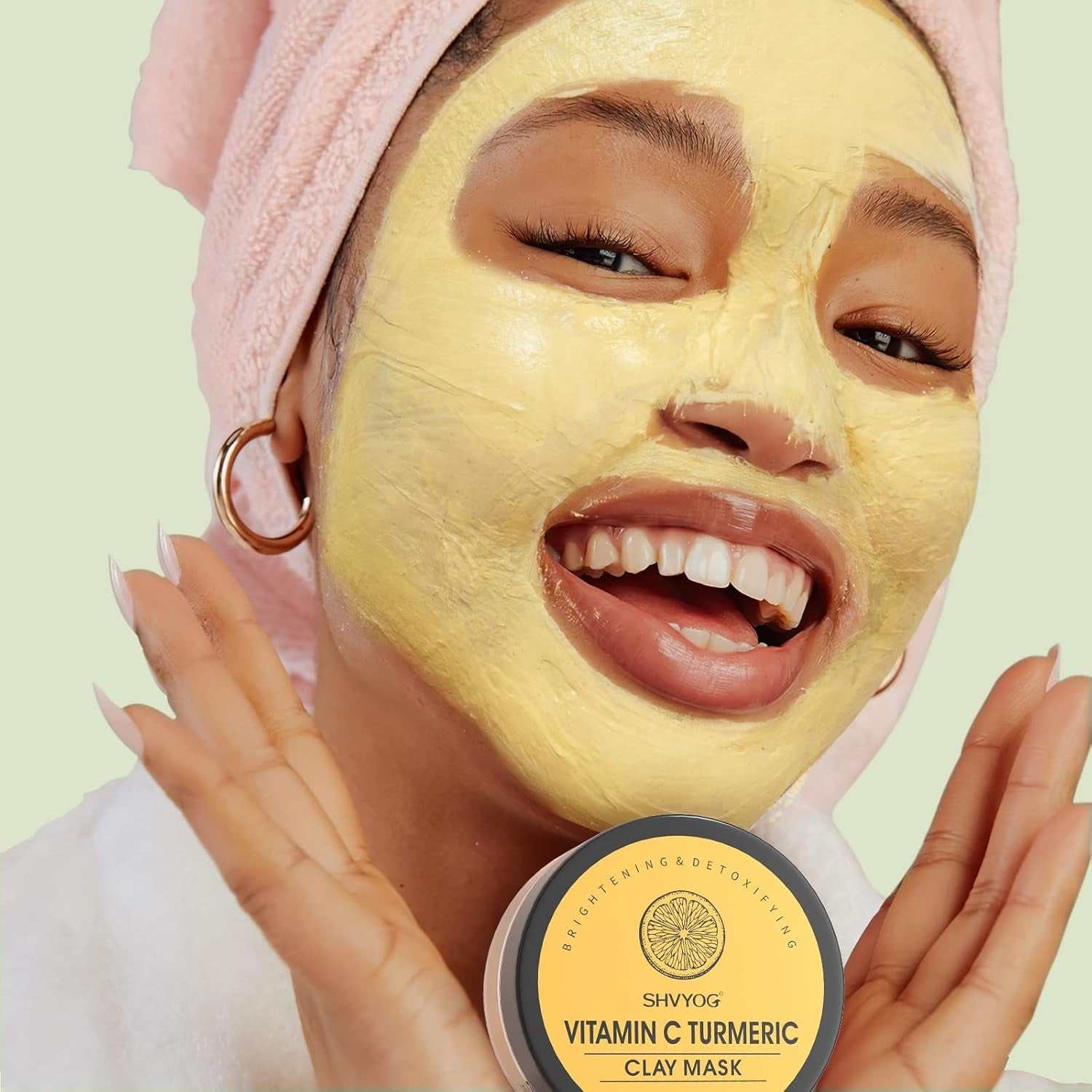 Young woman with a yellow clay facial mask and a jar labeled "Vitamin C Turmeric Clay Mask" in a skincare routine setting.
