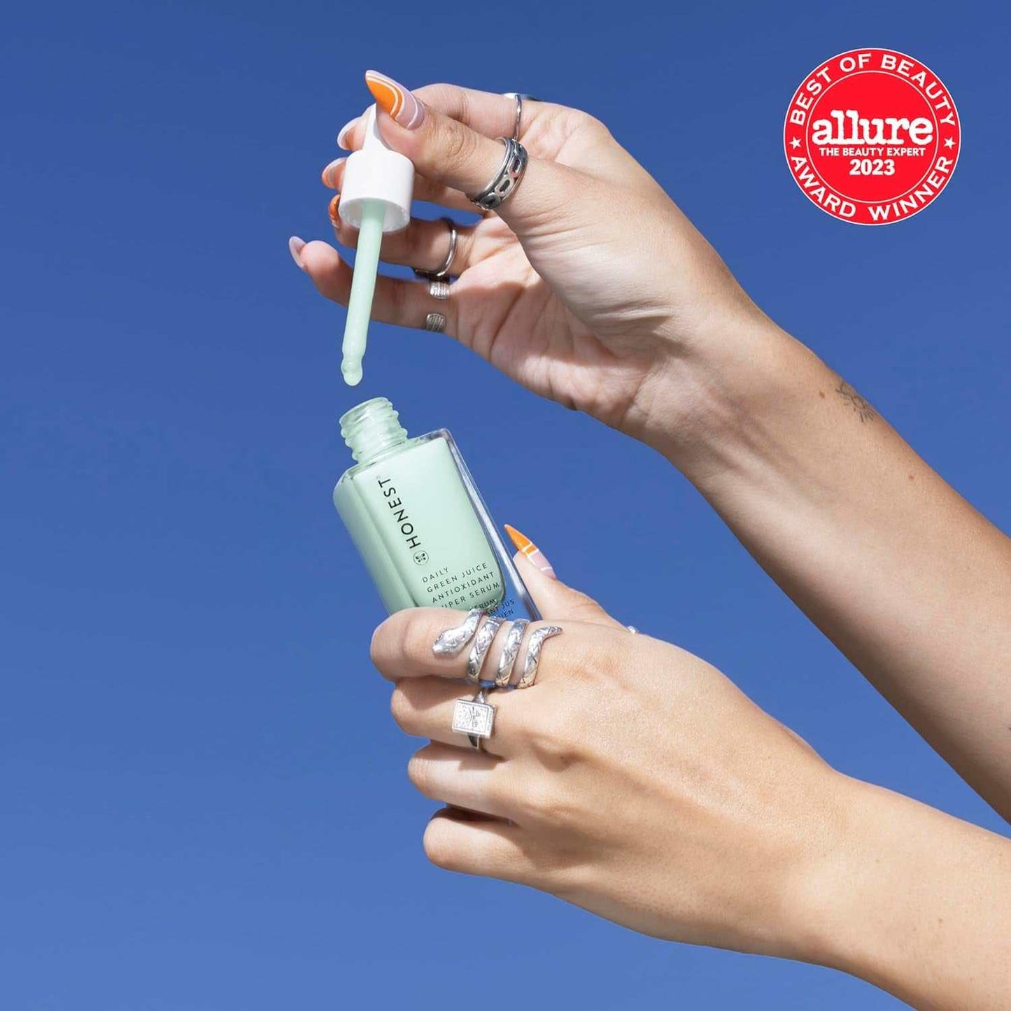 Person applying Cruelty-Free Antioxidant Super Serum with dropper, showing light green vegan serum bottle, Allure award badge visible.
