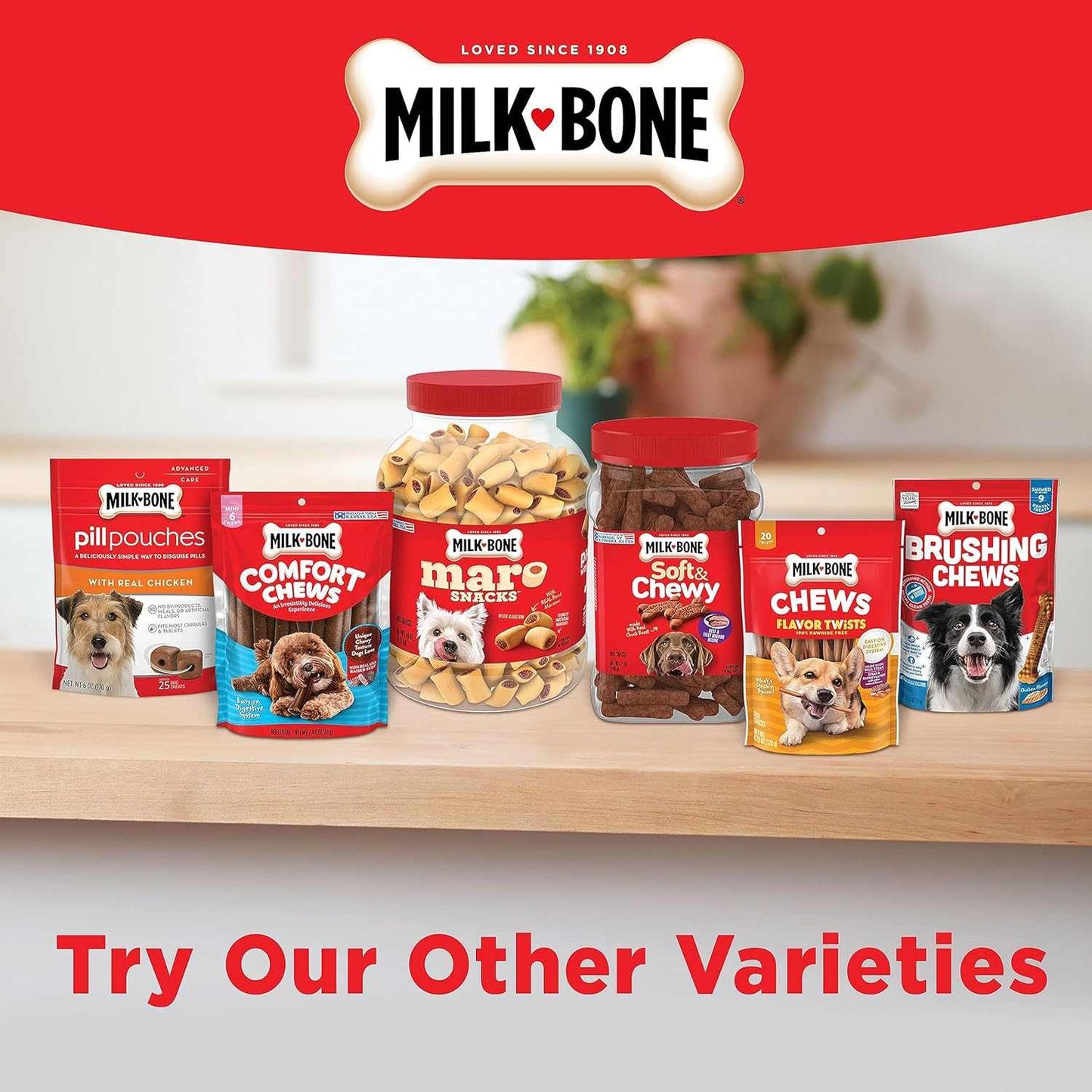 Assorted Milk-Bone dog treats including marrow-infused small dog treats, chews, and pill pouches displayed on a wooden surface with a red branded backdrop.