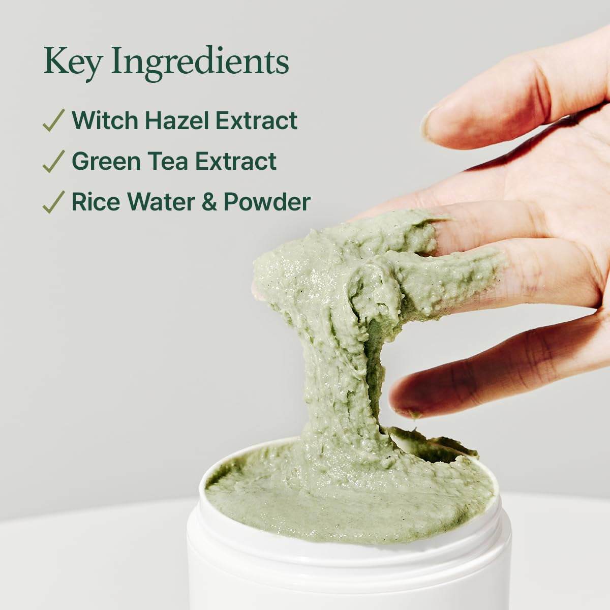 Hand scooping green creamy face cleanser with witch hazel, green tea, and rice water extracts in white jar