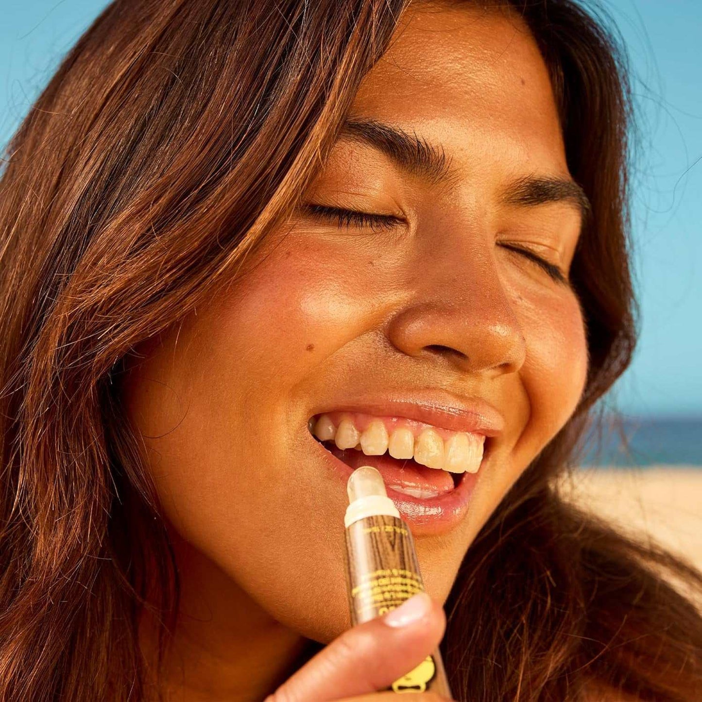 Woman applying reef-safe moisturizing sunscreen lip balm outdoors on a sunny day