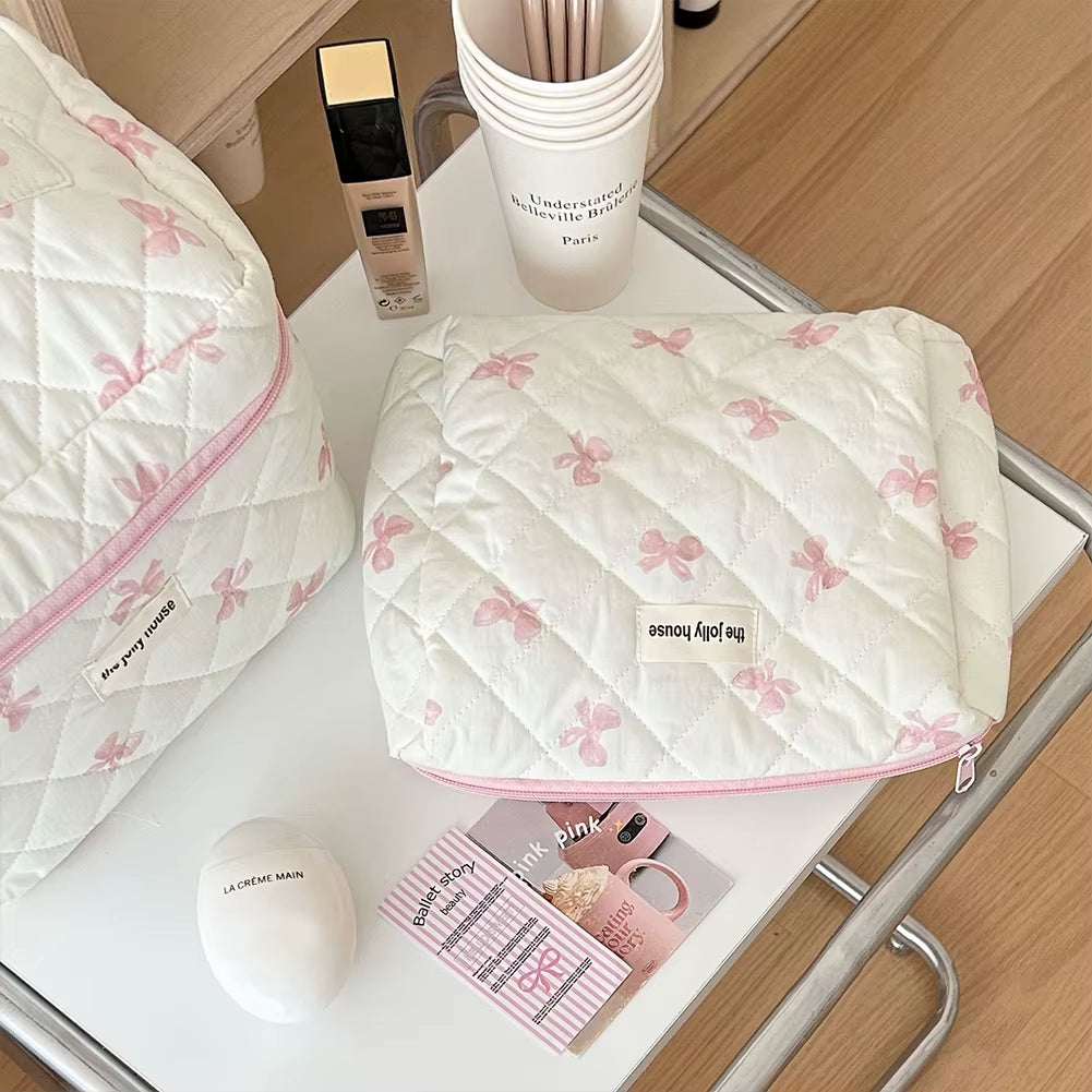 Quilted floral makeup bag with bow accents, ideal for travel and cosmetics storage on a white table.