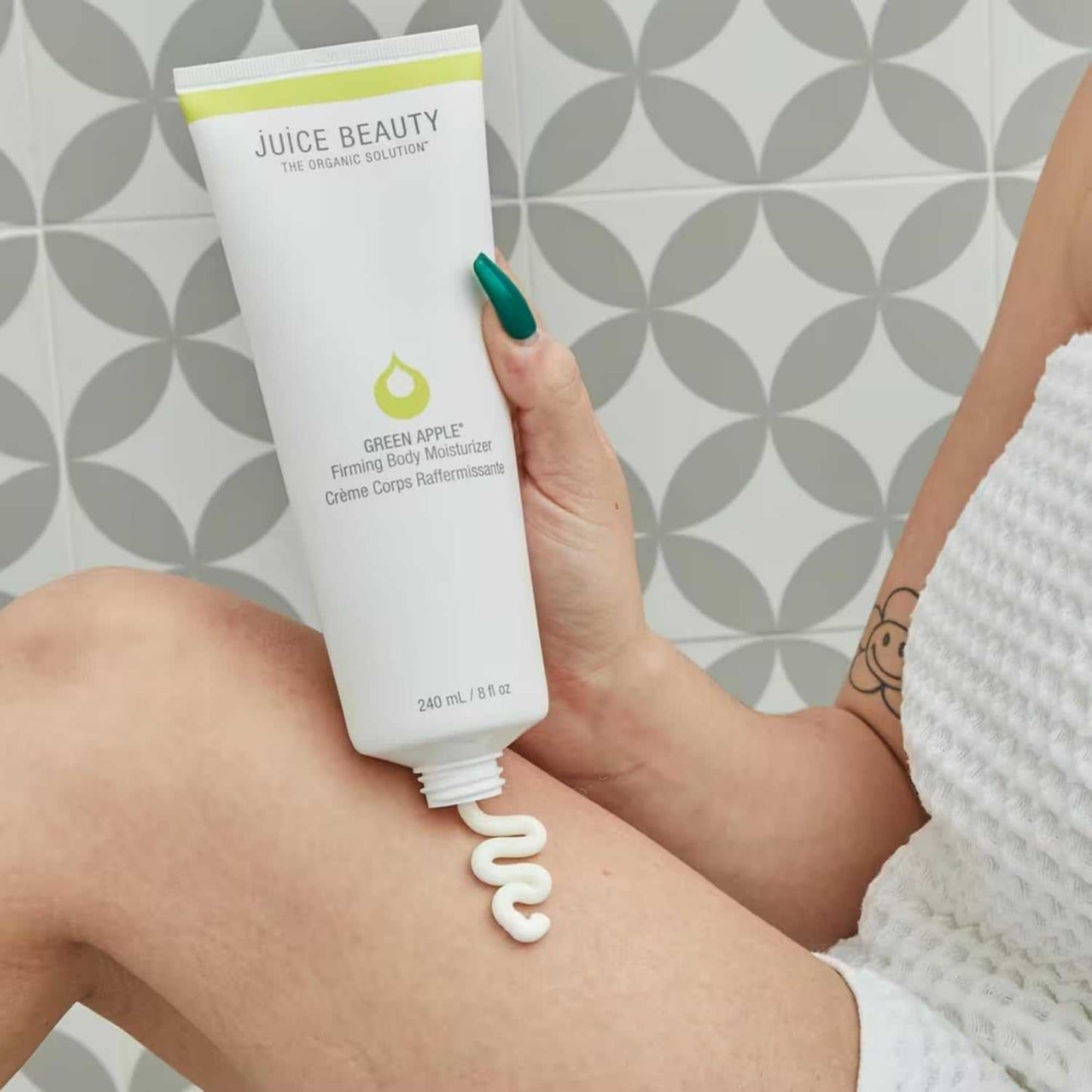 Green Apple Firming Body Moisturizer tube dispensing cream on leg with geometric background