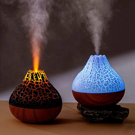 Two desktop electric USB air humidifiers shaped like volcanoes emitting mist with one glowing orange and the other blue with a cracked surface design