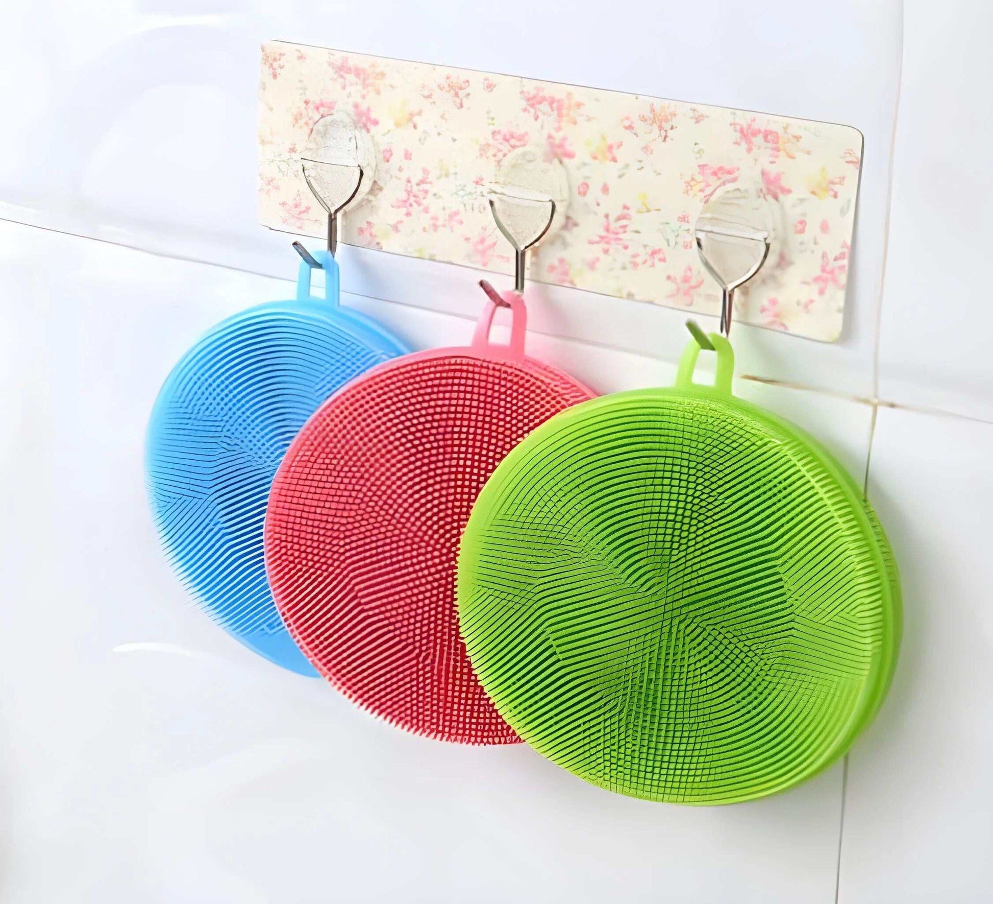 Eco-friendly magic silicone sponge scrubbers in blue, pink, and green hanging on hooks.