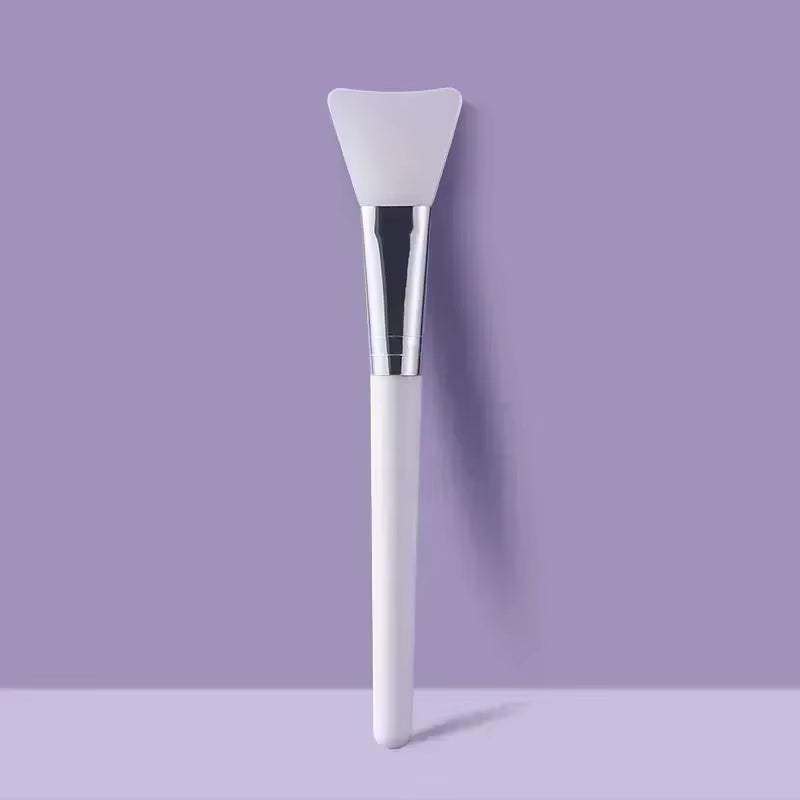 Silicone facial mask brush with flexible head and durable handle on a purple background.