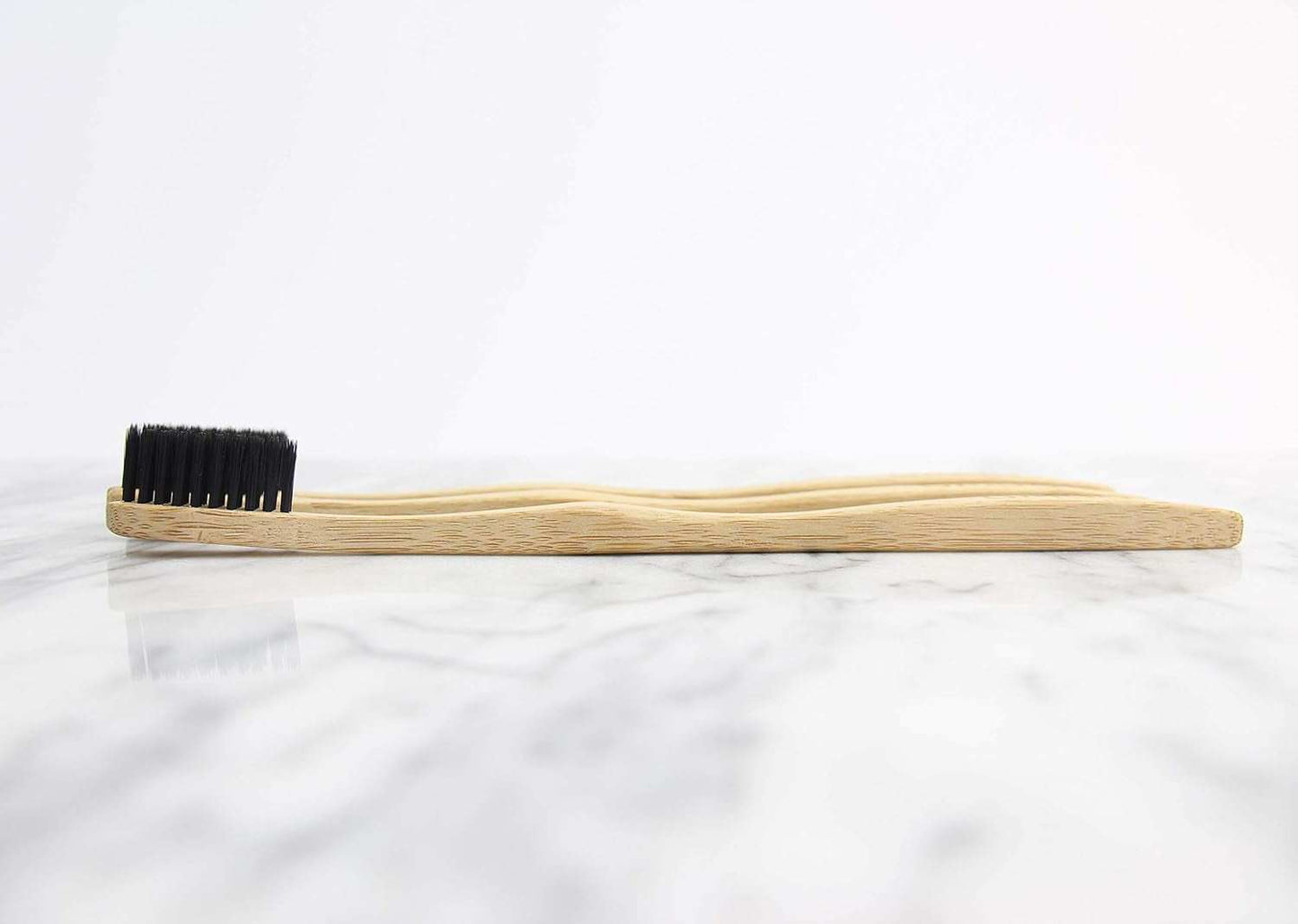 Wooden ToothBrush with charcoal bristles and bamboo handle on a marble surface.