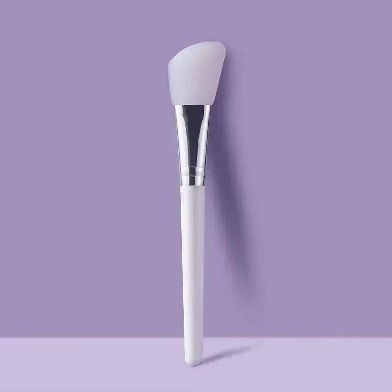 Silicone facial mask brush with a soft, flexible head and durable handle on a purple background.