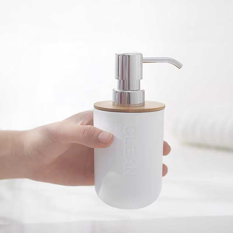 Hand holding a white soap dispenser with silver pump and bamboo lid for bathroom decoration