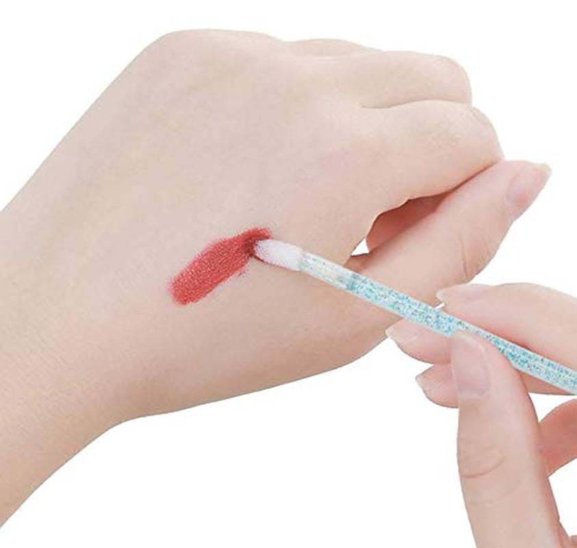 Disposable crystal lip brush applying lipstick swatch on hand.