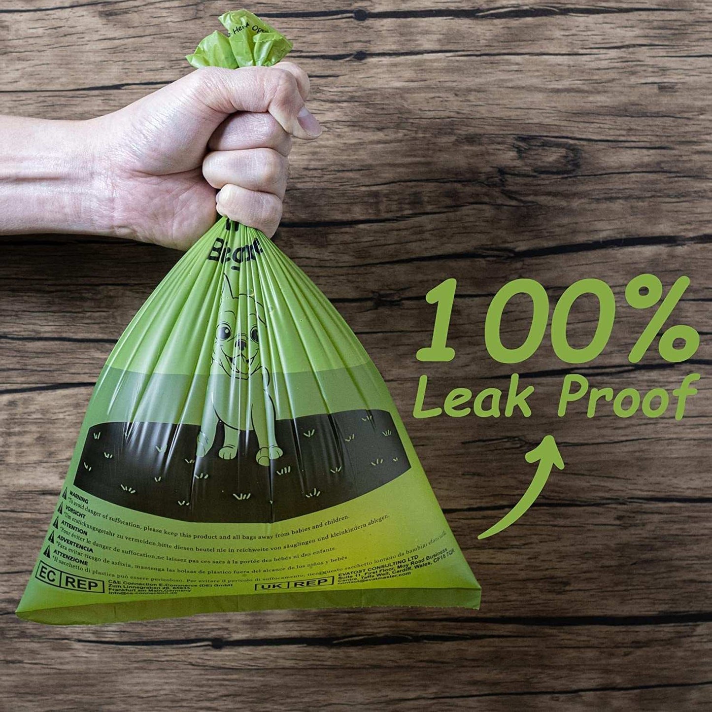 Hand holding a green, 100% leak-proof poop bag for dog waste against a wooden background