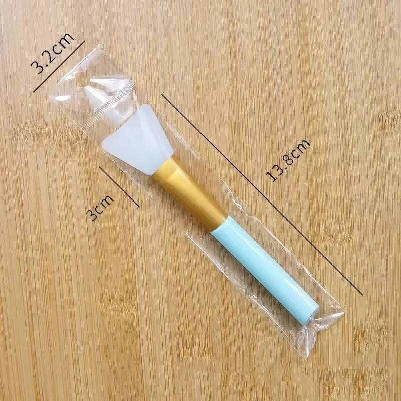 Silicone facial mask brush with gold and blue handle, packaged in clear wrap, ideal for skincare applications.